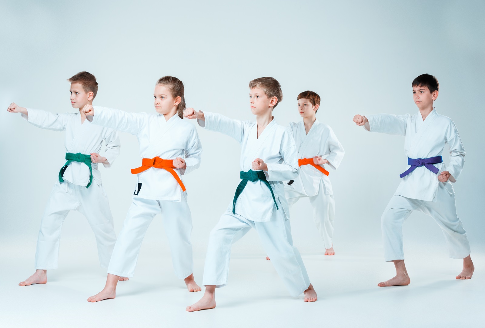 Fünf Kinder üben Judo, jedes trägt einen Gürtel in einer anderen Farbe